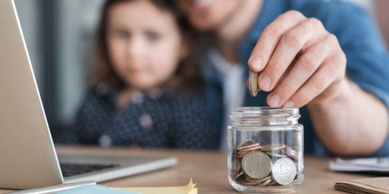 man and daughter putting coins into a jar